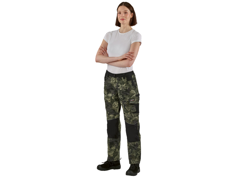 Donna in pantaloni da lavoro mimetici e maglietta bianca con le braccia incrociate.