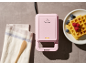 Piastra per waffle rosa con spia luminosa, canovaccio e waffle con frutti di bosco.