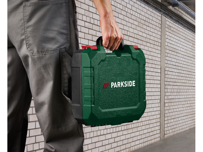 Persona in abiti da lavoro che tiene una cassetta degli attrezzi verde con scritte bianche.