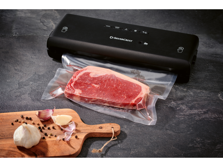 Macchina sottovuoto con un pezzo di carne confezionato e aglio su un tagliere.