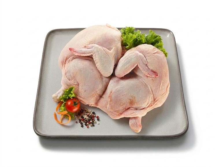 Due polli interi crudi con spezie e verdure su un vassoio grigio.