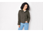 Donna con giacca verde militare e jeans blu, sorridente alla fotocamera.