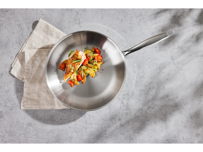 Padella con pollo e verdure su sfondo di cemento con canovaccio.