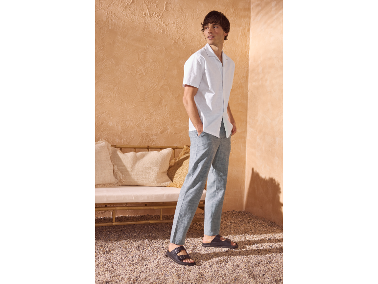 Uomo in camicia bianca e pantaloni grigi, in piedi su un pavimento di ciottoli.