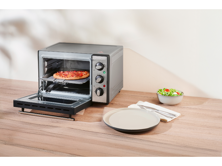 Mini forno con pizza, pronto per essere servito con insalata e piatto.