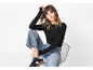 Donna con top nero a maniche lunghe, jeans a gamba larga e sneakers seduta su una sedia.