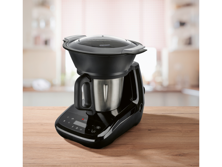 Robot da cucina nero con ciotola in acciaio inossidabile e coperchio trasparente su tavolo in legno.