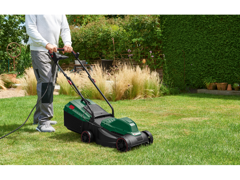 Uomo che taglia il prato con un tosaerba elettrico in un giardino soleggiato.