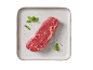 Pezzo di carne di manzo cruda con erbe e spezie su un piatto chiaro.