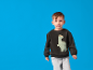 Bambino sorridente in felpa scura con stampa dinosauro e pantaloni della tuta grigi