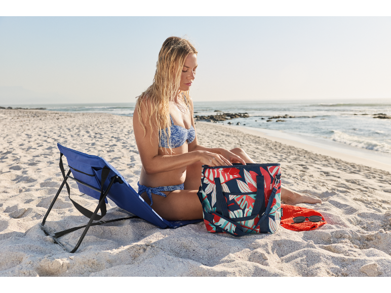 Donna in spiaggia con una sedia da spiaggia e una borsa frigo.