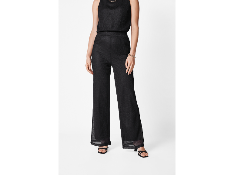 Donna con pantaloni neri ampi e top senza maniche, con sandali con tacco.