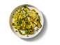Patate e zucchine grigliate con salsa pesto e foglie di basilico su un piatto bianco.