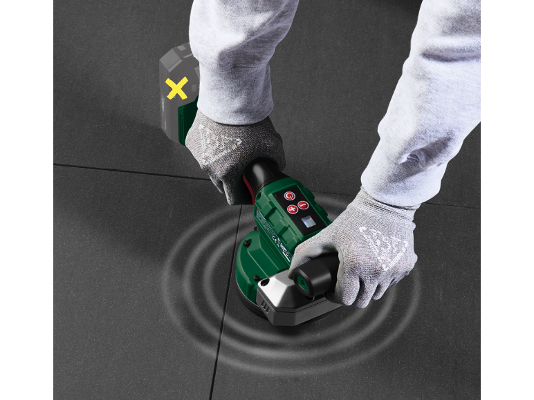 Uomo con guanti usa un vibratore per piastrelle su piastrelle scure.