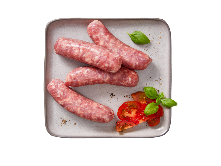 Salsicce crude con pomodori a fette e foglie di basilico su un piatto.