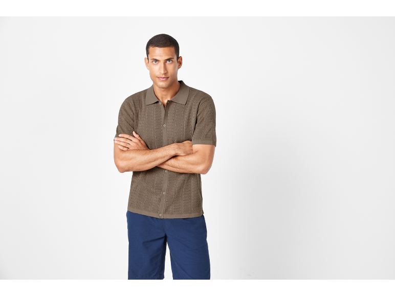 Uomo con polo in maglia marrone e pantaloncini blu, a braccia conserte.