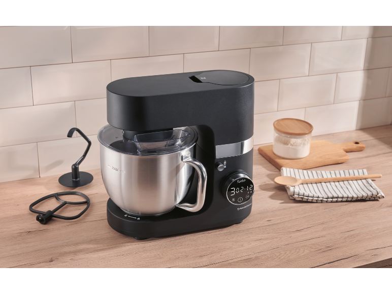 Robot da cucina nero con ciotola in acciaio inossidabile, accessori e ingredienti da forno.