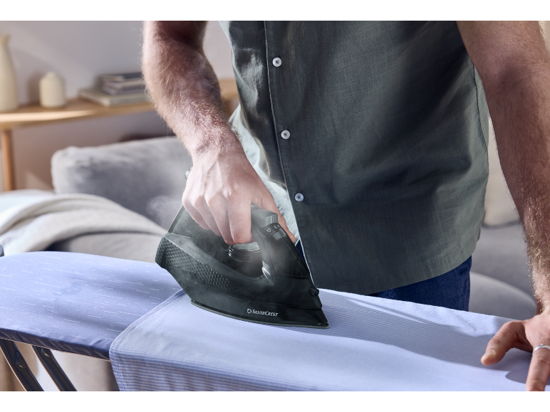 Una persona stira una camicia azzurra su un asse da stiro con un ferro scuro.