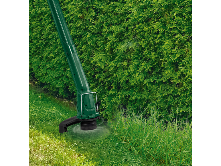 Un tagliabordi verde taglia l'erba alta vicino a una siepe.