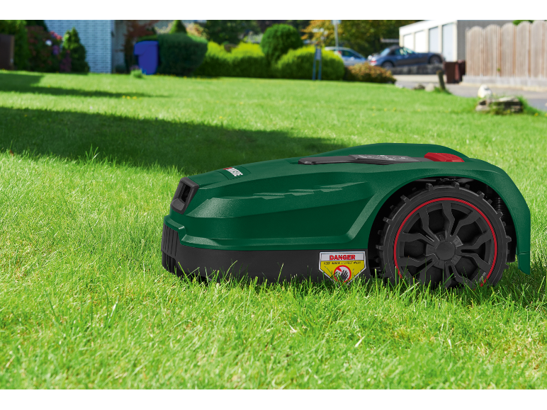 Robot tagliaerba su erba verde con adesivo di avvertenza.