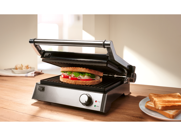 Panino in una piastra per panini aperta su un tavolo di legno.