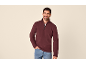 Uomo con felpa bordeaux a mezza zip e jeans, sorridente.