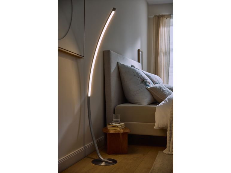 Lampada da terra a LED curva in una camera da letto moderna con letto e comodino.