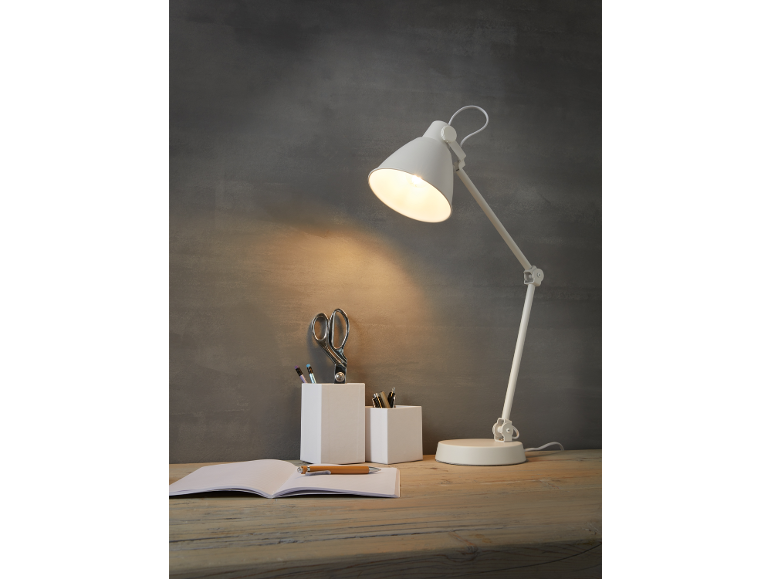 Lampada da scrivania bianca illumina una scrivania con un quaderno, penne e forbici.