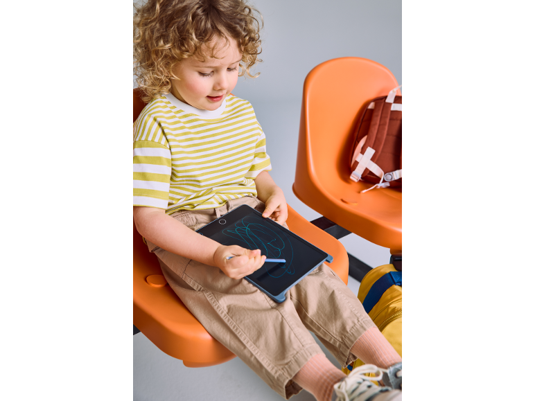 Bambino che disegna su una tavoletta digitale, seduto su una sedia arancione.