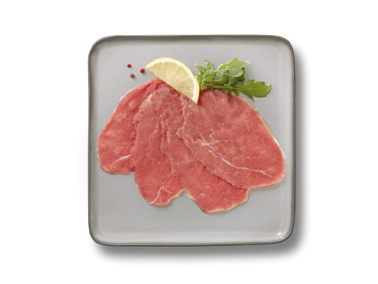 Fettine sottili di carne di manzo con limone e rucola su un piatto grigio.
