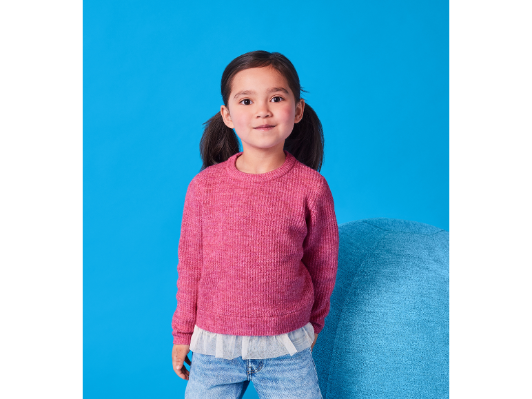 Bambina con maglione rosa a maglia e jeans, sorridente su sfondo blu.