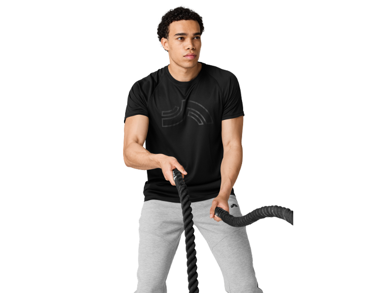 Uomo in t-shirt sportiva nera e pantaloni della tuta grigi che tiene le corde da battaglia.