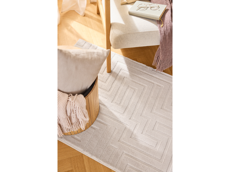 Tappeto chiaro con motivo geometrico, poltrona e contenitore in legno.