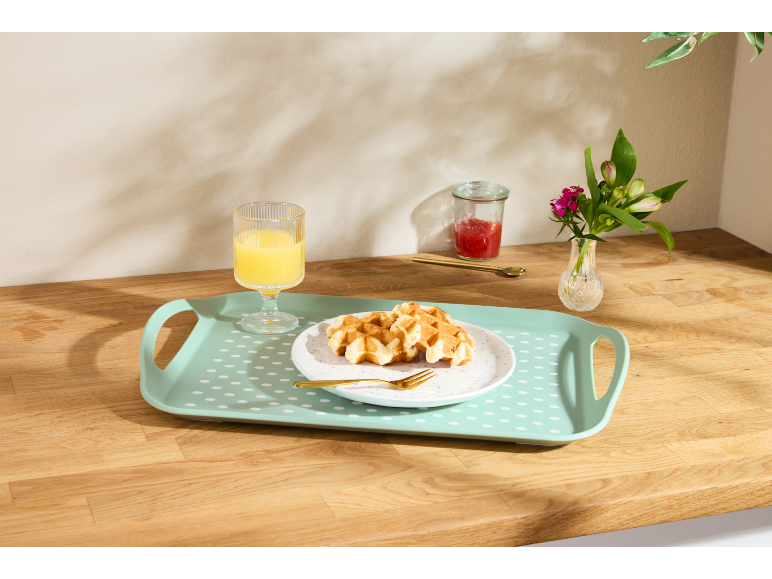 Vassoio con waffle, succo d'arancia, marmellata e fiori su un bancone di legno.