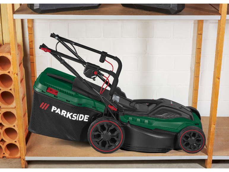 Tosaerba verde con sacco di raccolta, riposto su uno scaffale di legno in garage.