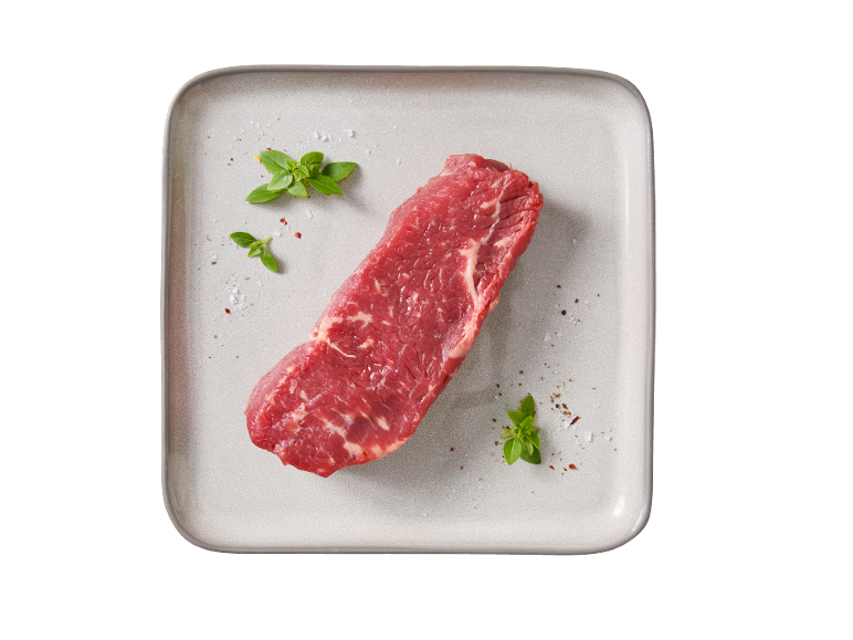 Pezzo di carne di manzo cruda con erbe e spezie su un piatto chiaro.