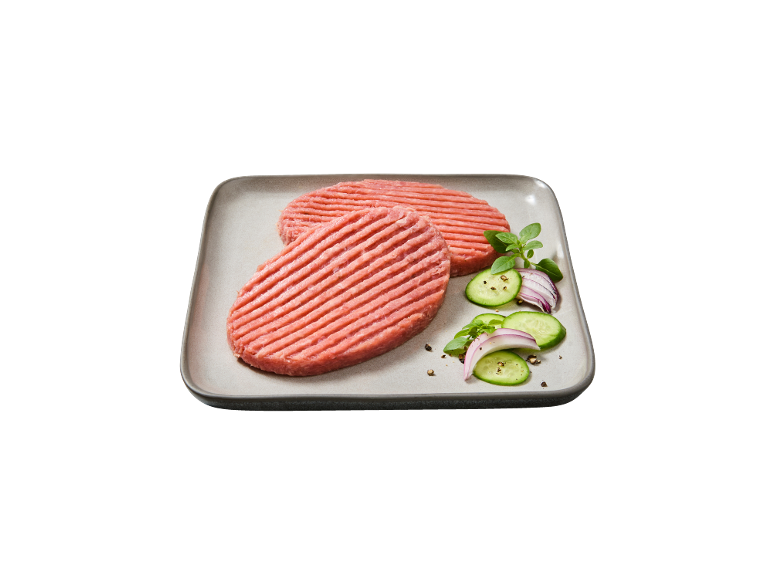 Due hamburger crudi con cetrioli, cipolla rossa ed erbe aromatiche su un piatto.
