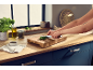 Persona che trita prezzemolo su un tagliere di legno in cucina con erbe e olio.