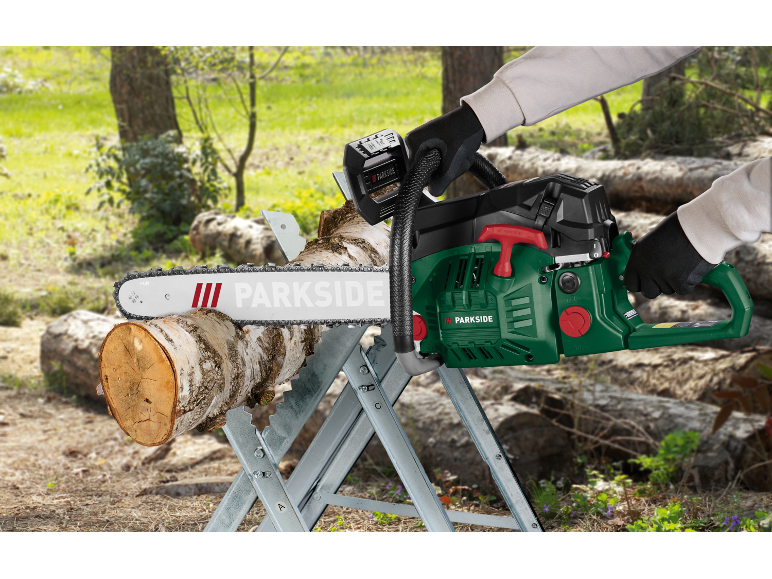Motosega a batteria verde che taglia un tronco di legno su un cavalletto in un ambiente esterno.