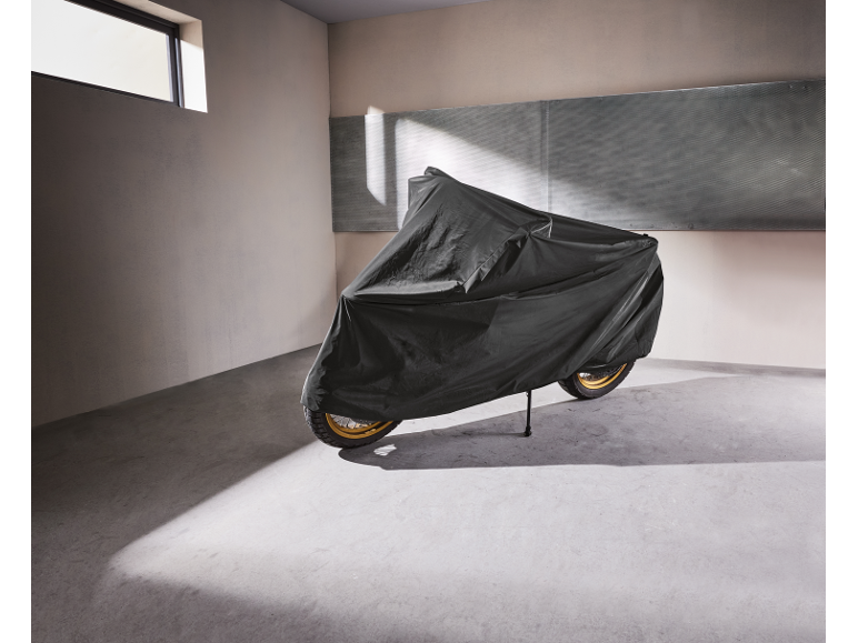 Motocicletta coperta da un telo protettivo in un garage con luce solare.