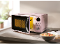 Forno a microonde rosa con porta aperta e ciotola di pasta sul bancone della cucina.