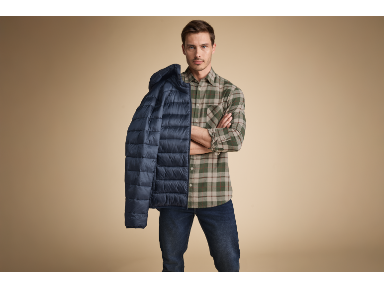 Uomo in camicia a quadri che tiene una giacca piumino blu sulla spalla.