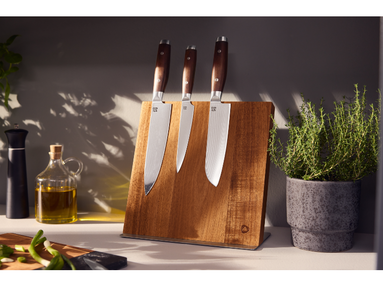 Tre coltelli da cucina con manici in legno su un supporto magnetico in legno in cucina.