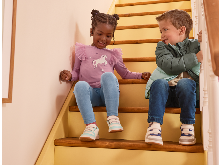 Due bambini in abbigliamento casual e scarpe da ginnastica seduti su scale di legno, sorridendo.