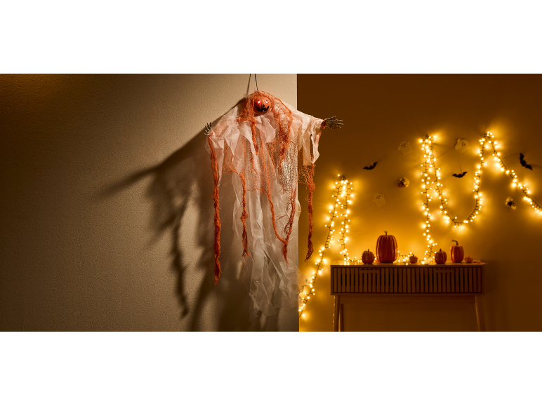 Decorazione di Halloween: fantasma con testa di zucca, luci a stringa e zucche su un tavolo.