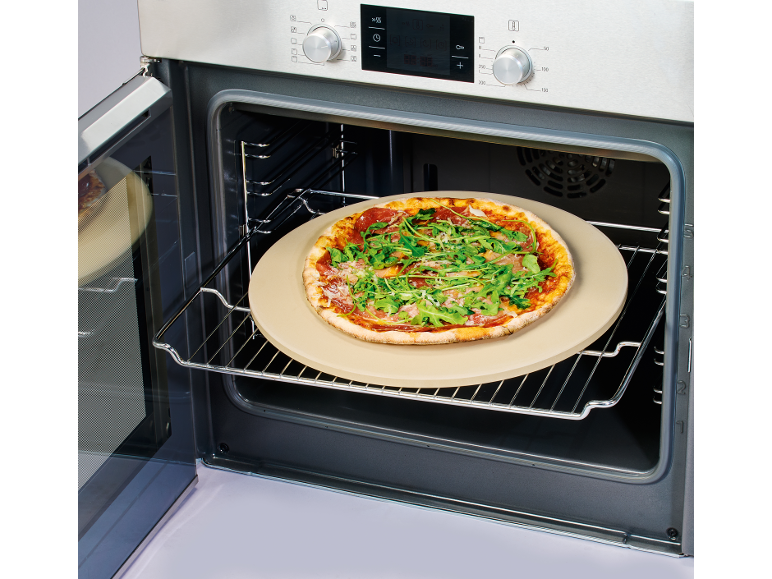 Pizza appena sfornata con rucola e prosciutto su pietra refrattaria in un forno aperto.