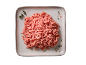 Carne macinata cruda su un piatto grigio chiaro, guarnita con erbe e spezie.
