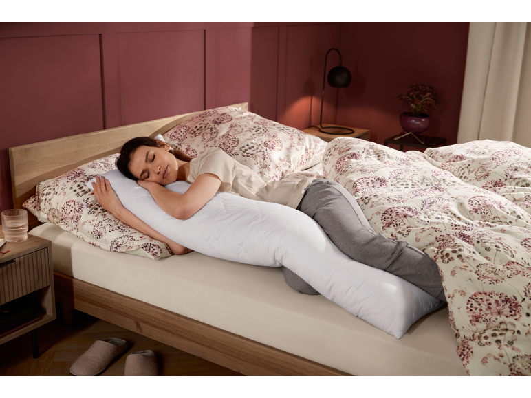 Donna dorme su un fianco nel letto con un cuscino per il corpo e biancheria da letto floreale.