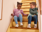 Due bambini in abbigliamento casual e scarpe da ginnastica seduti su scale di legno, sorridendo.