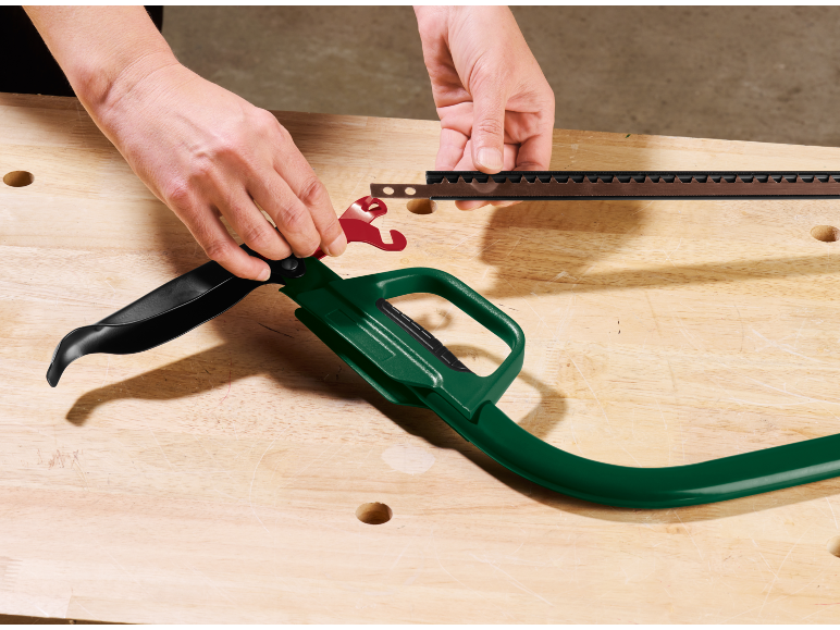 Mani che assemblano una lama di sega su un manico verde su un banco da lavoro in legno.